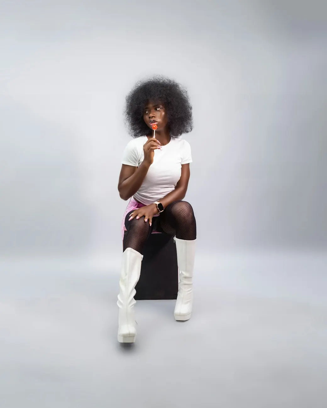 Woman with an afro in white boots posing on a stool