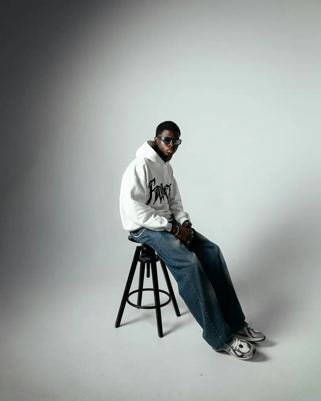 Man in a white hoodie seated on a stool in a grey studio