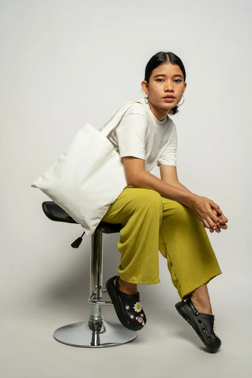 Woman on a studio stool with a canvas tote and olive trousers