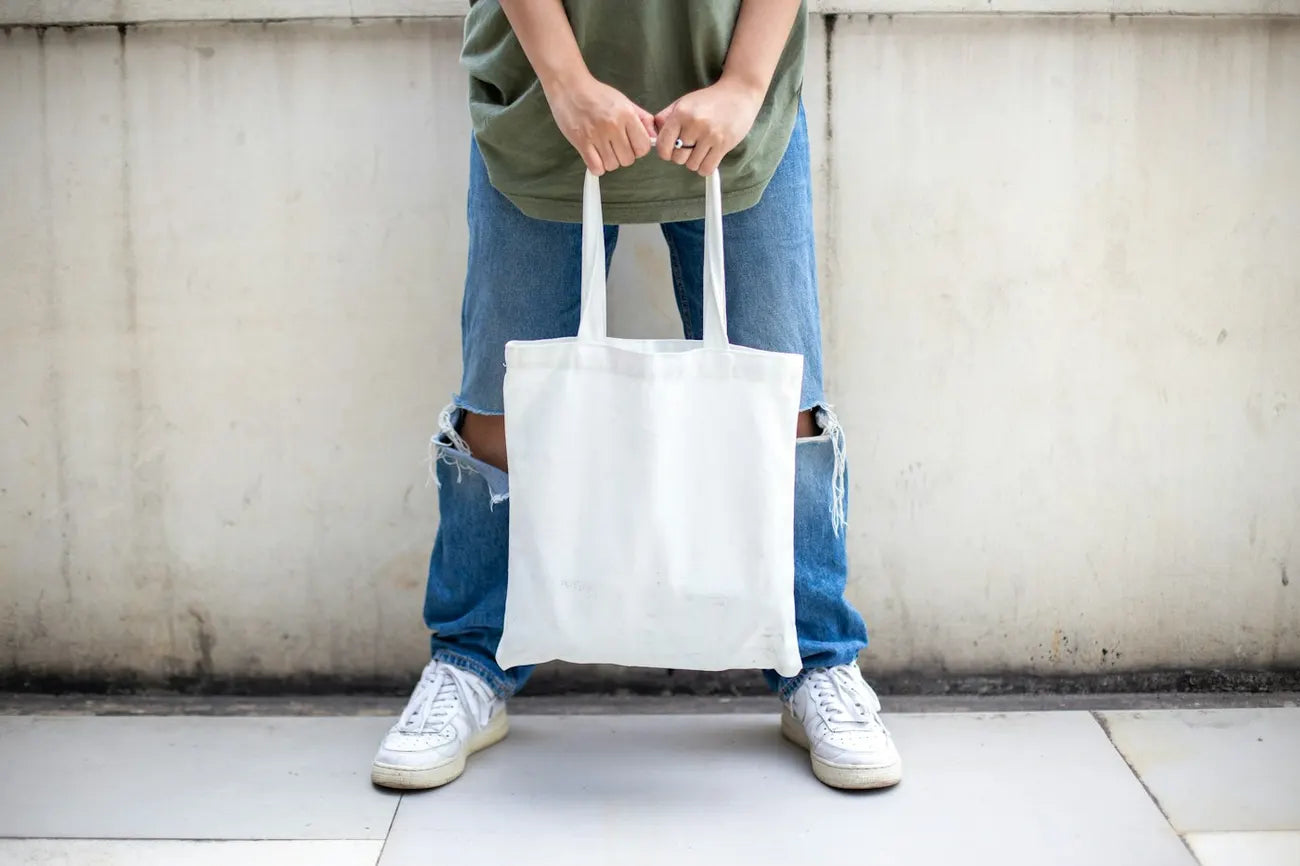 Hands holding a plain canvas tote in front of denim